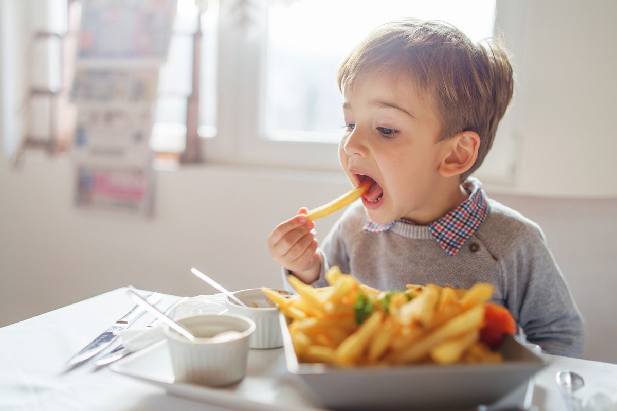 Jonge jongen zittend aan een tafel, die een friet eet van een bord vol friet, met dipsauzen in de buurt.