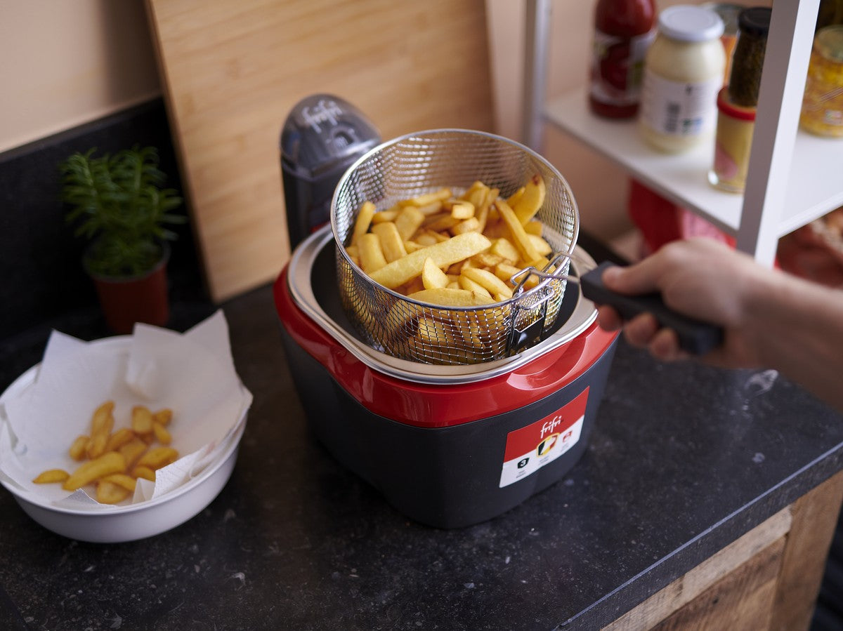 Une friteuse de comptoir avec une garniture rouge, remplie de frites cuites dans un panier en métal.