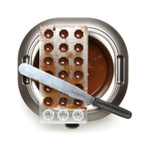 Un plateau de moulage La Chocolatière et une spatule reposent sur un bol de chocolat fondu, vu d'en haut.