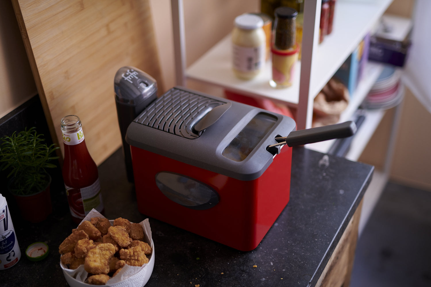Friteuse rouge et grise sur comptoir noir.