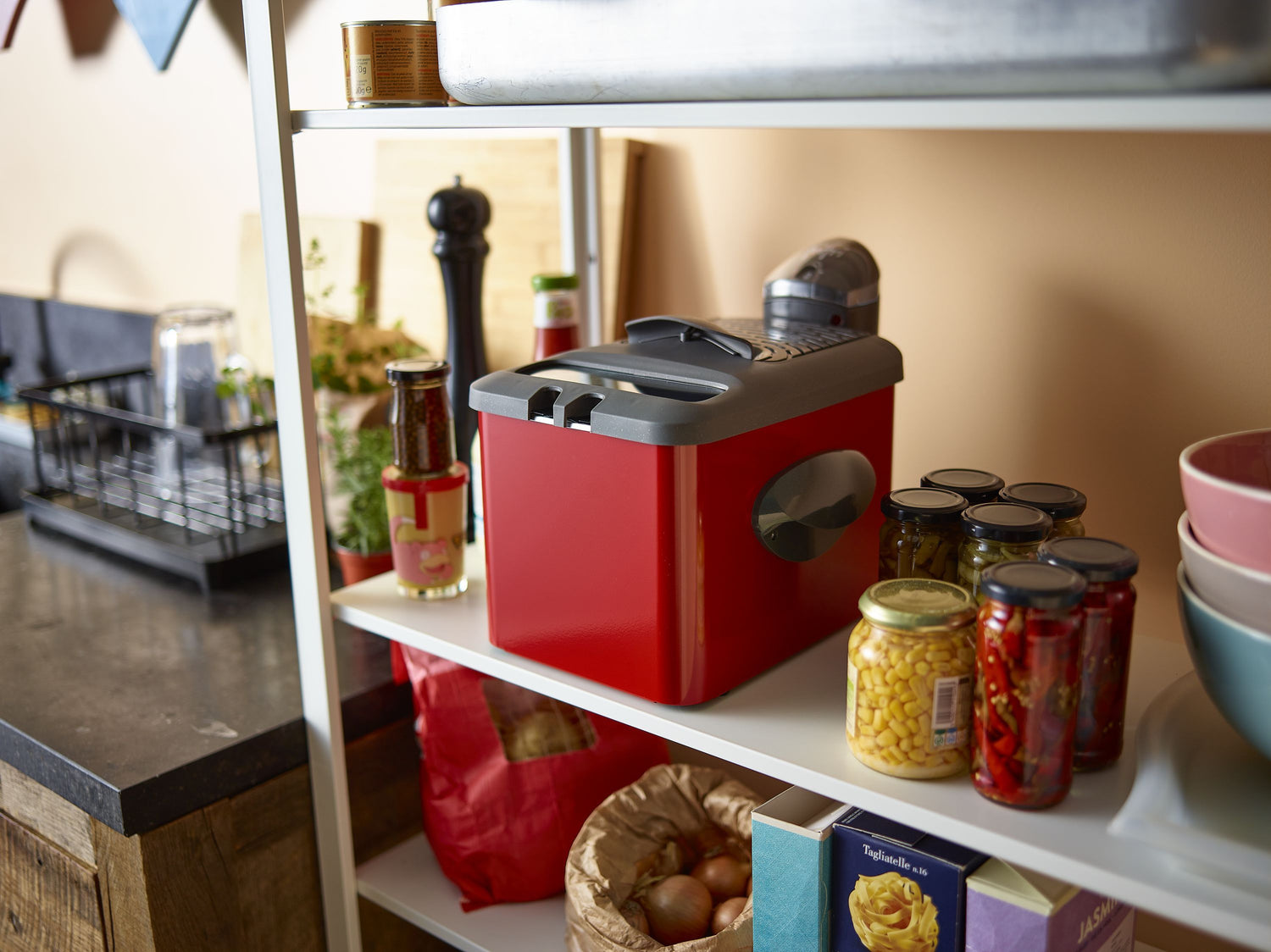 Étagère avec friteuse rouge, bocaux de conserves et provisions.
