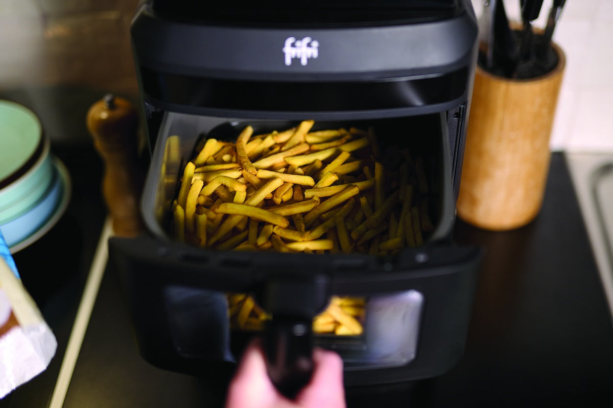 Une personne sort un panier de frites cuites d'une friteuse dans une cuisine.