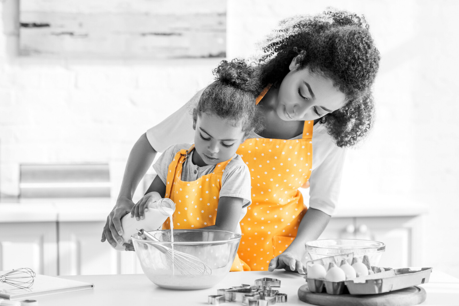 african american mother and daughter preparing dough and pouring milk into bowl in kitchen